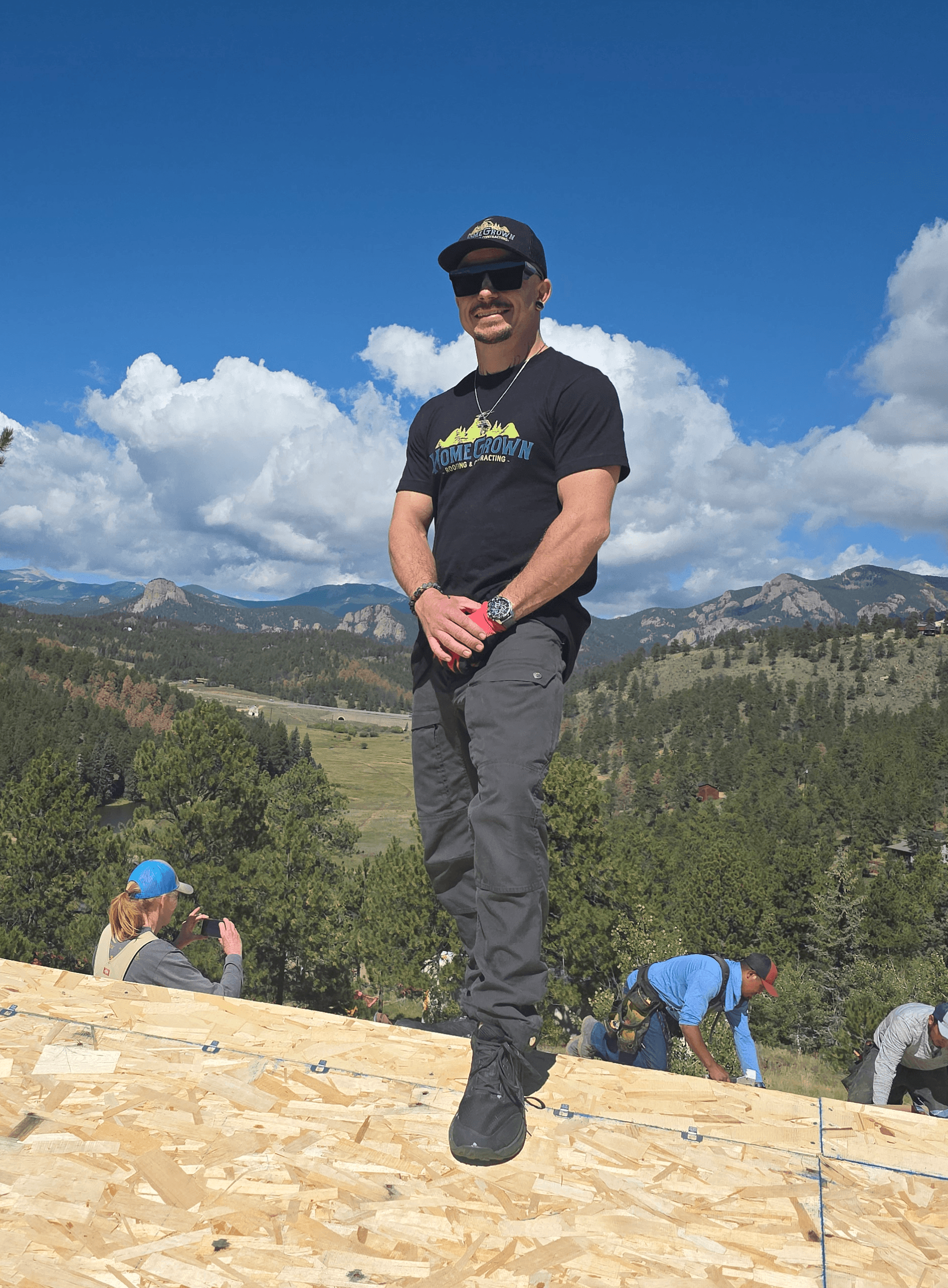 Person standing outdoors on a wooden surface with mountains and blue sky in background.