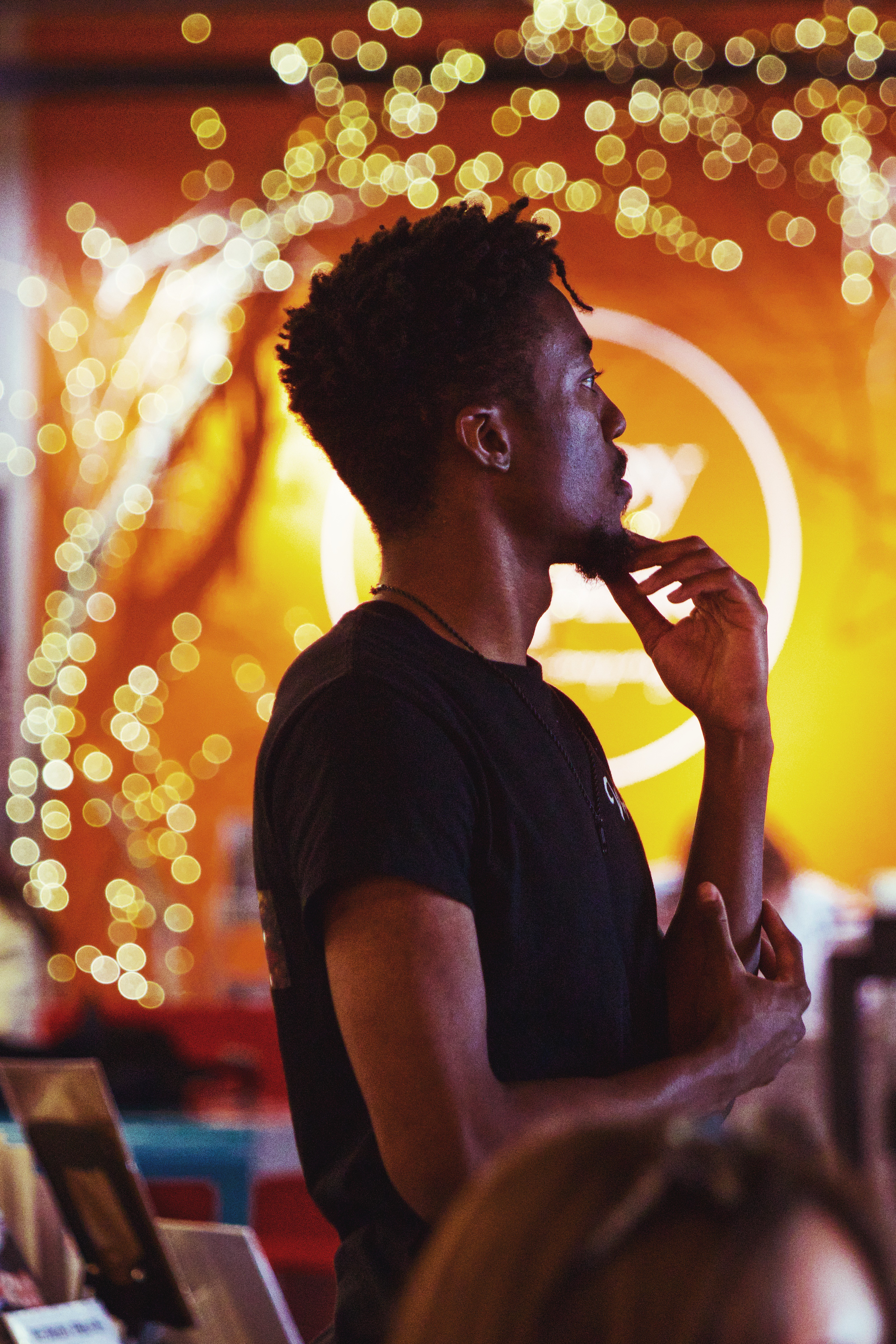 Side profile of a young man with curly hair, standing in front of a bright, festive background with lights.