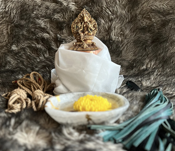 Decorative object on white cloth, bowl with yellow flower, and fabric strands on furry background.