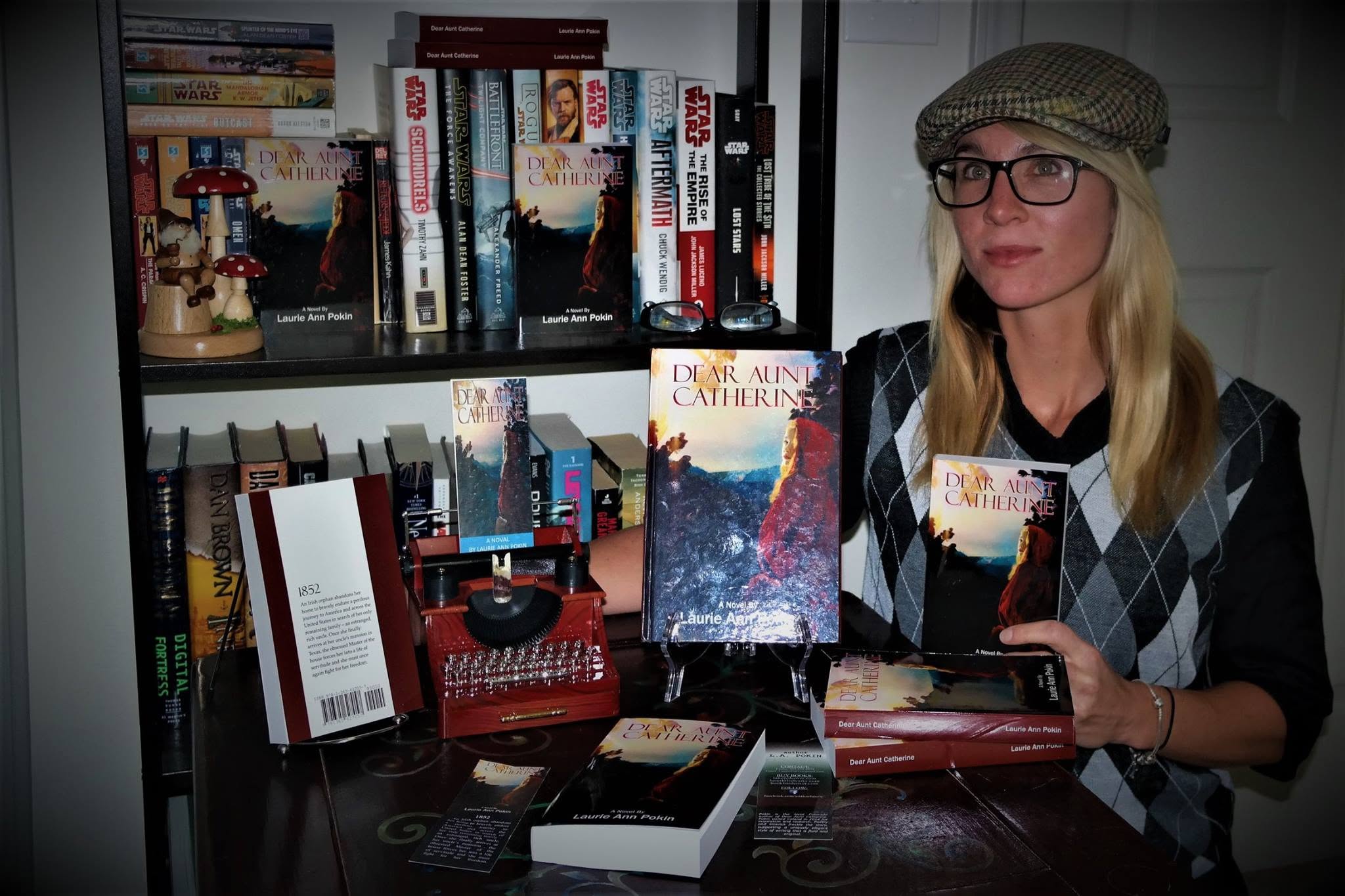 Woman with glasses and a hat sitting at a table with books and a vintage red telephone, bookshelf in background.