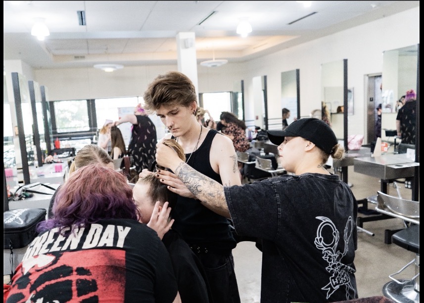 A makeup artist applies makeup to a young woman in a salon with large windows and mirrors.