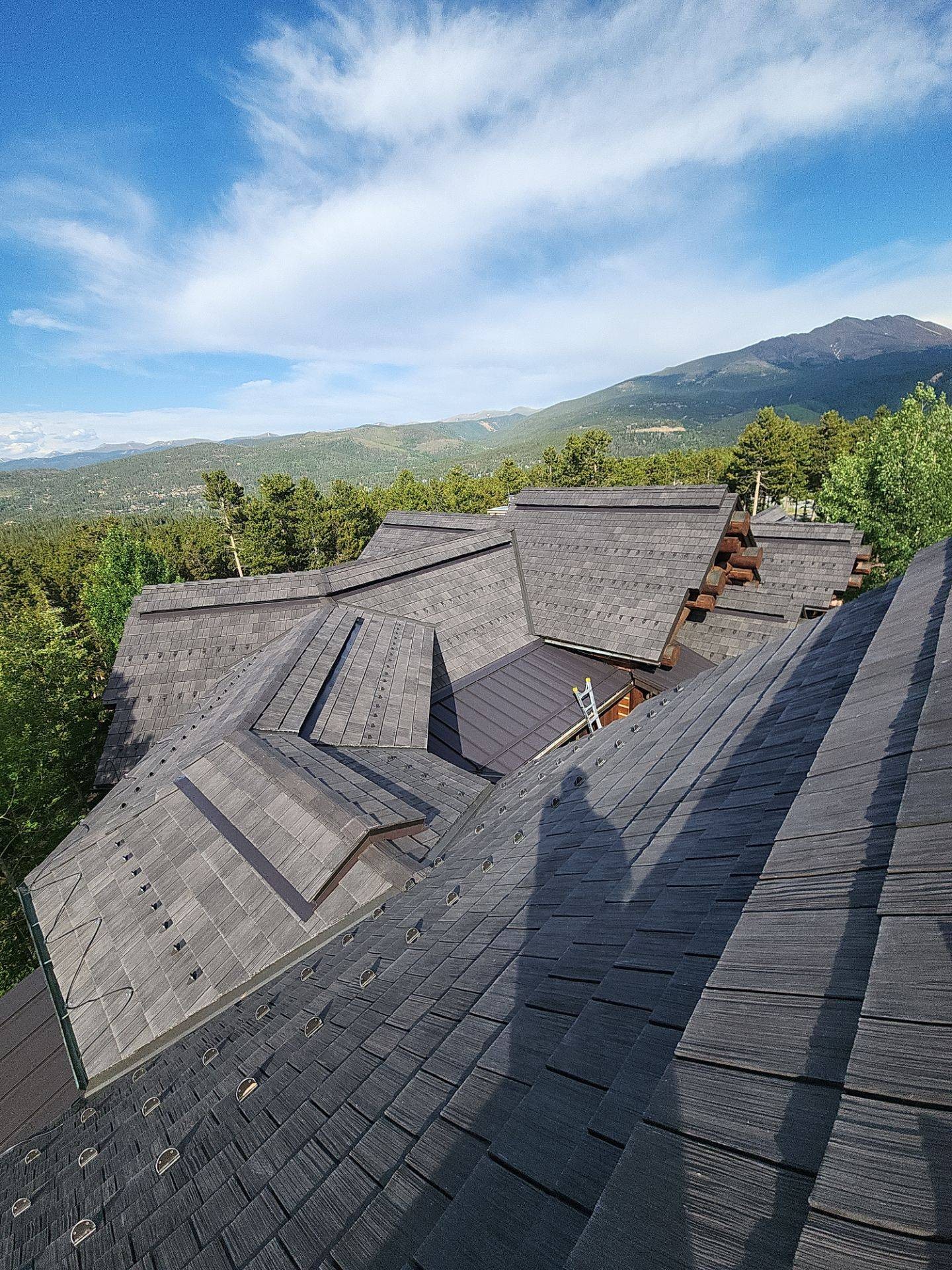 View of rooftops with mountains and sky in the background, shadow of a person in the foreground.