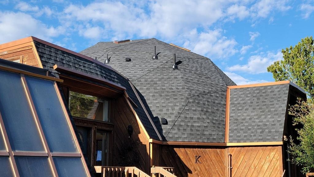 View of rooftops with a blue sky and clouds, including a house with dark shingles and wooden siding.