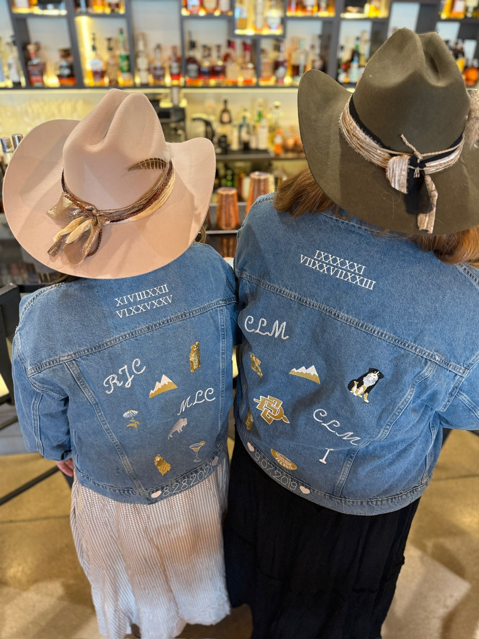Two people wearing denim jackets and wide-brimmed hats, standing in a store with shelves of bottles in the background.