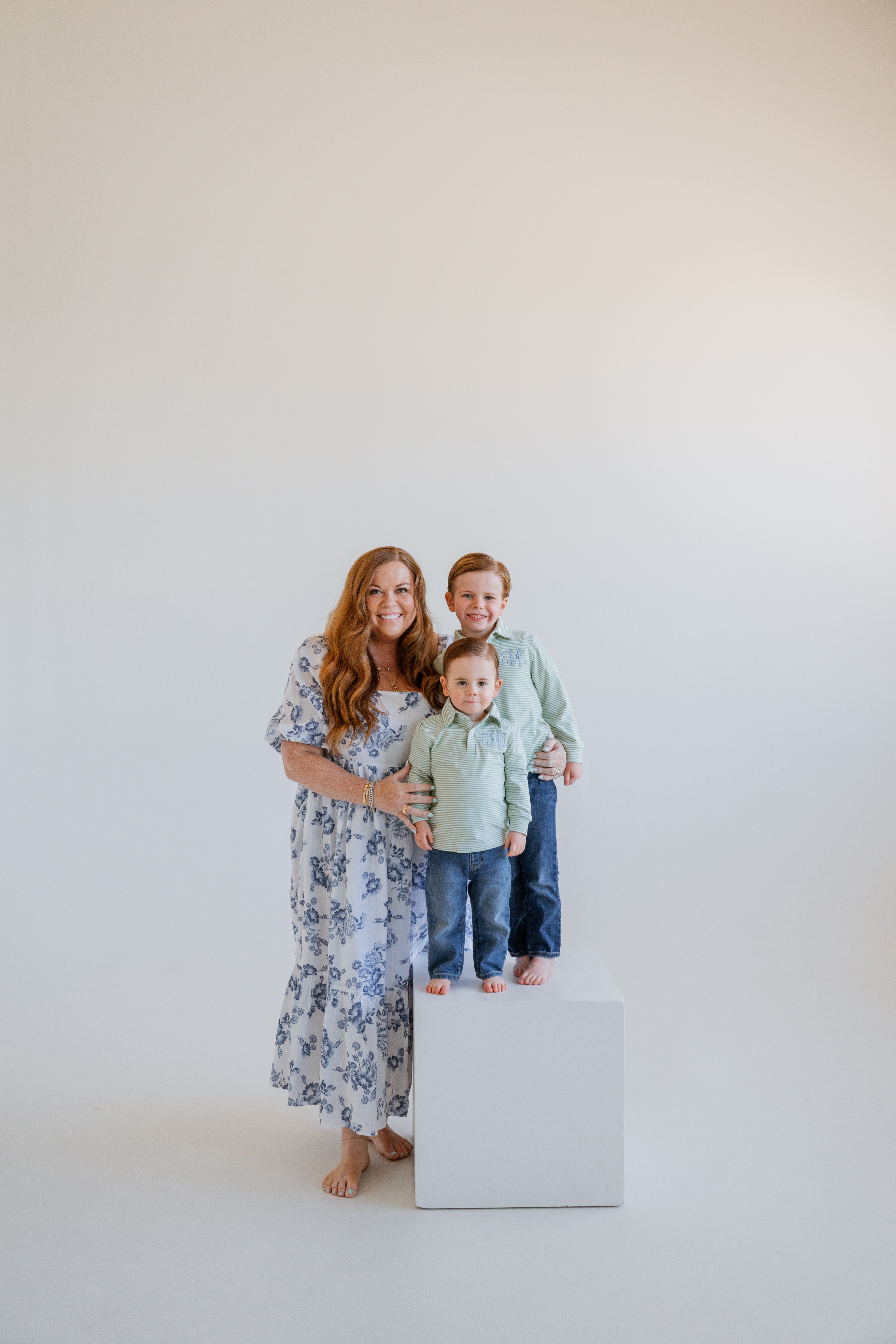 Three people, a woman and two children, stand together on a white platform against a plain light background.
