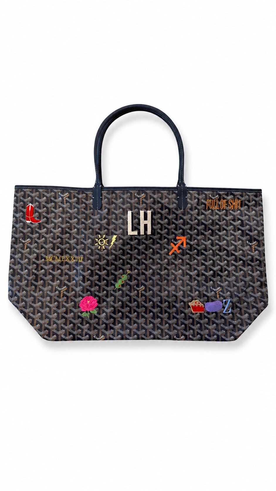 Black tote bag with colorful embroidered patches and gold initials, handles at top, on a white background.