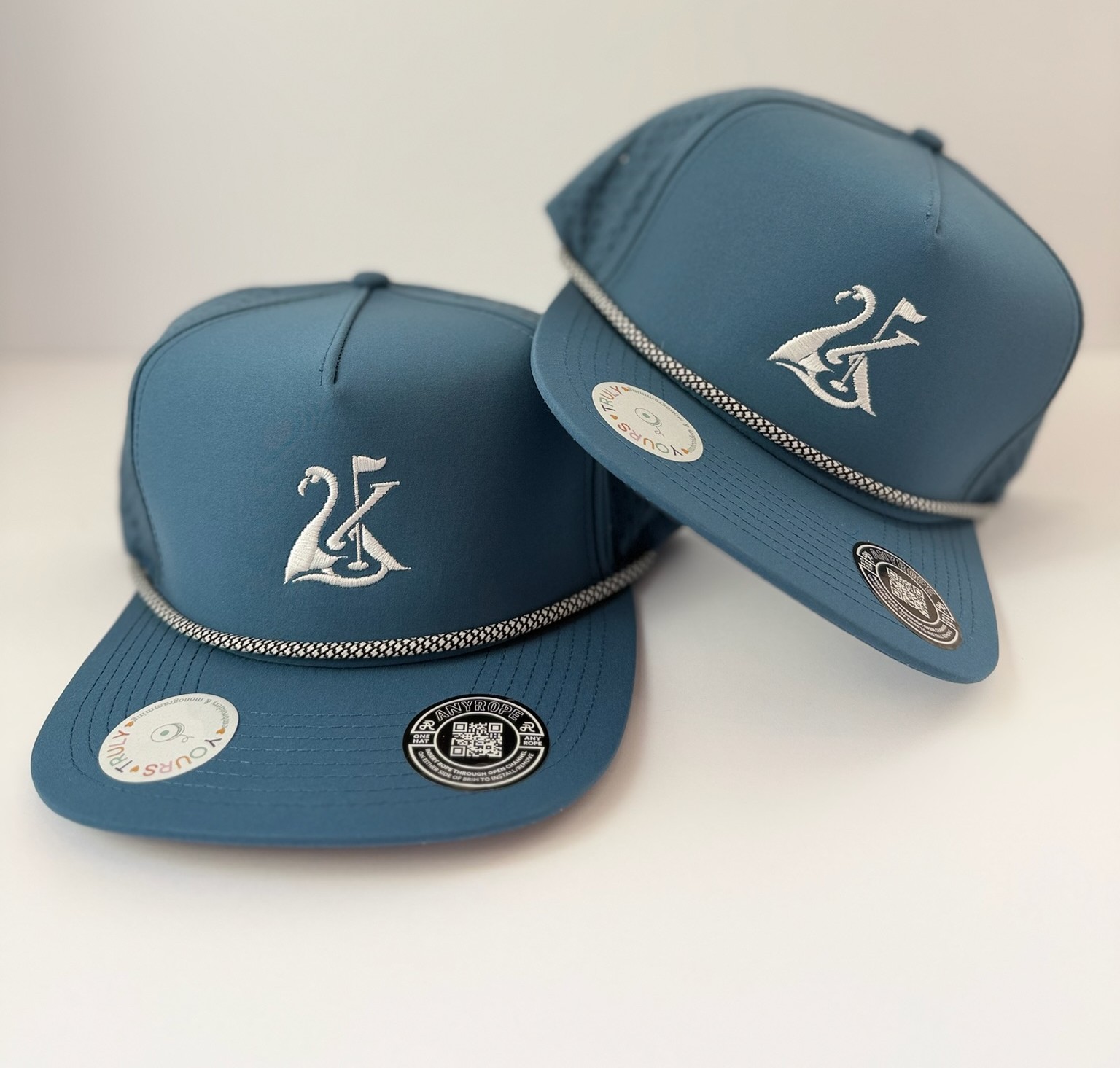 Two blue baseball caps with logos and stickers, placed on a white surface.