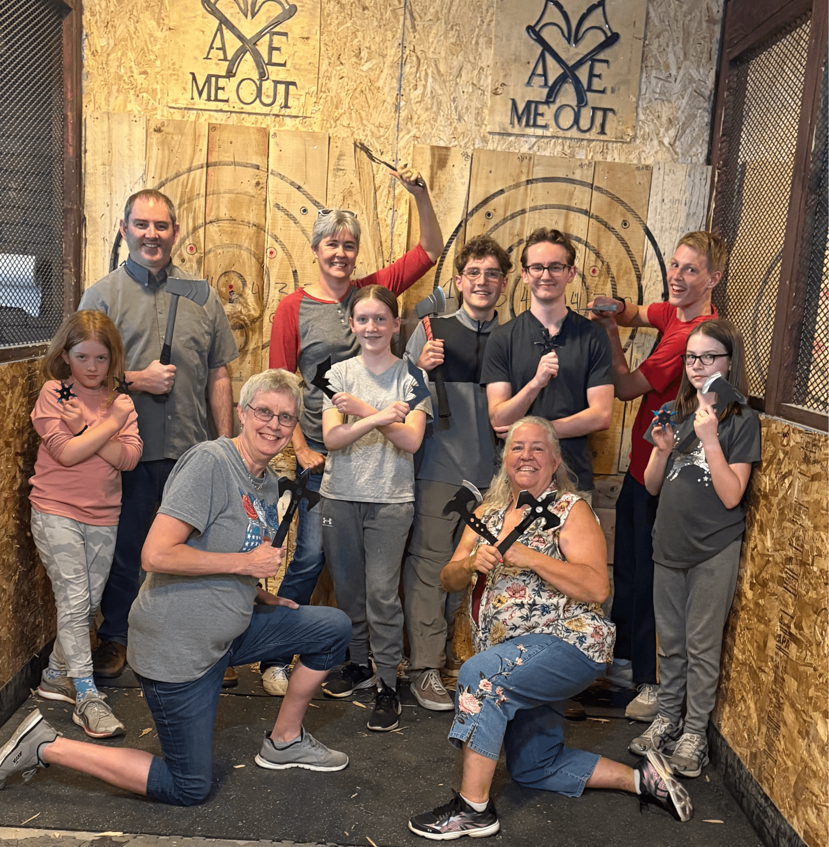 Group of ten people, some holding axes, posing indoors with wooden targets and banners in the background.