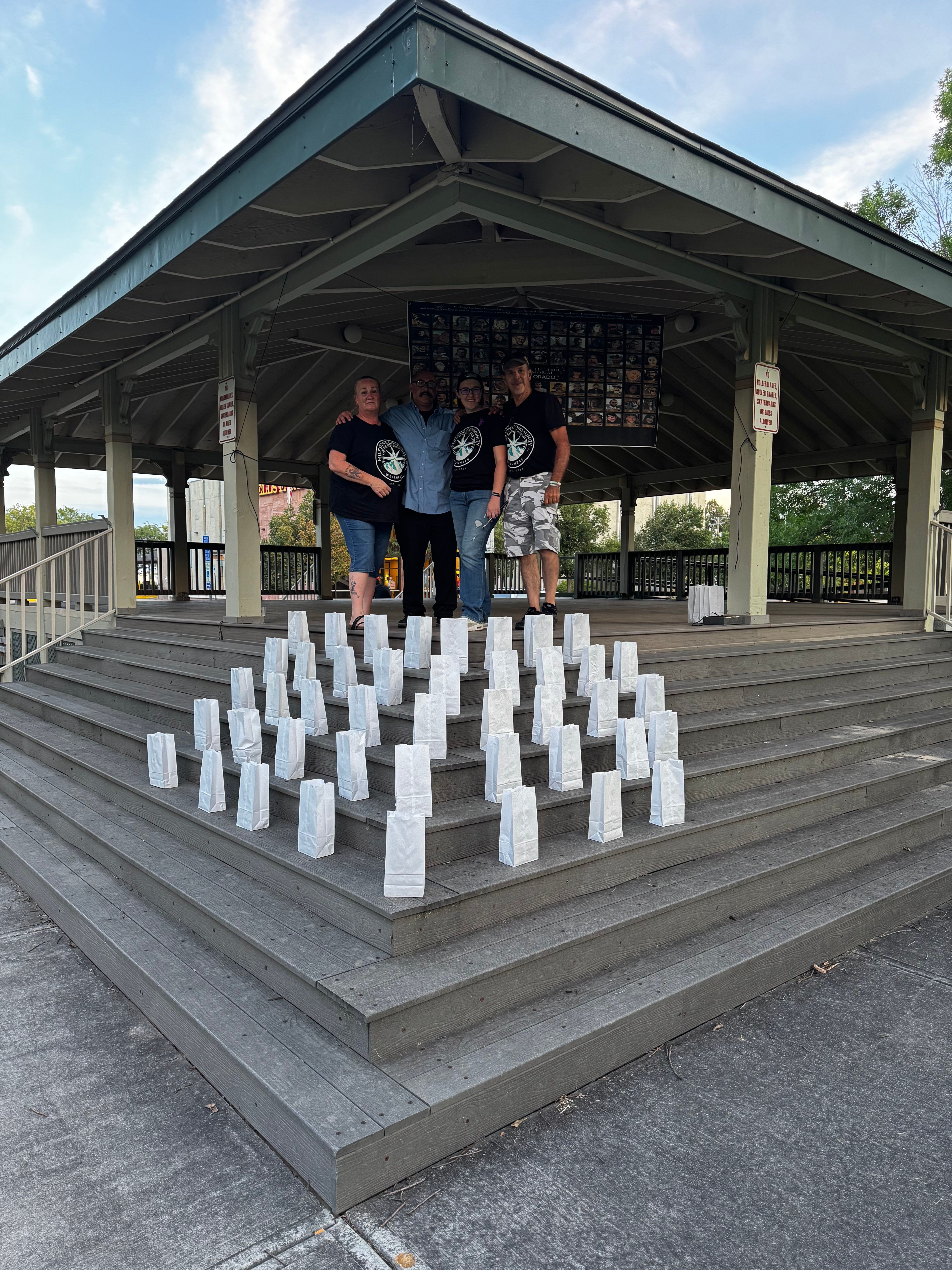 People standing on steps near a building with white blocks arranged on the steps, under a roofed area with trees in background.