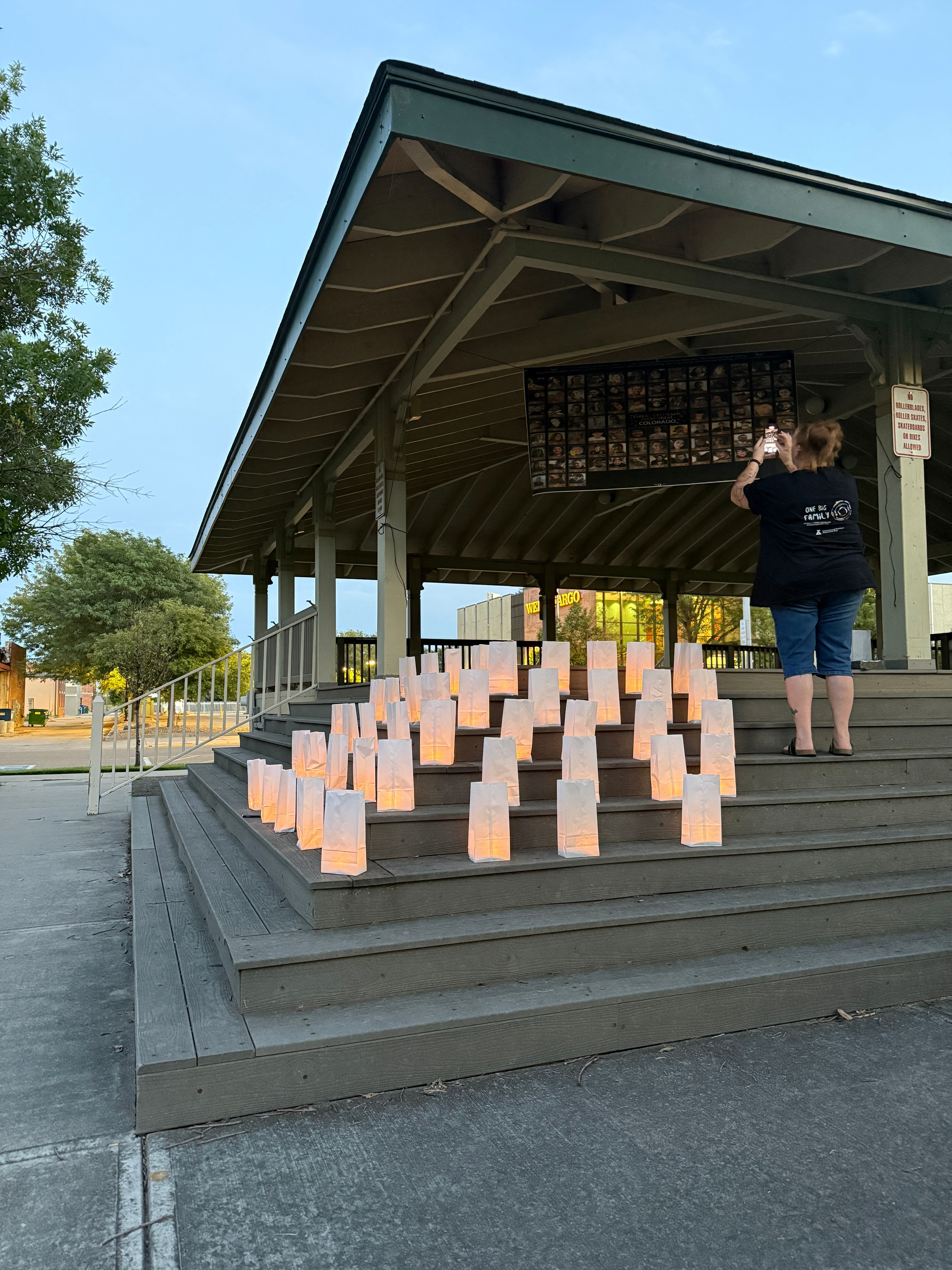 Person standing on steps near a display of pink paper blocks, with trees and a building in the background.