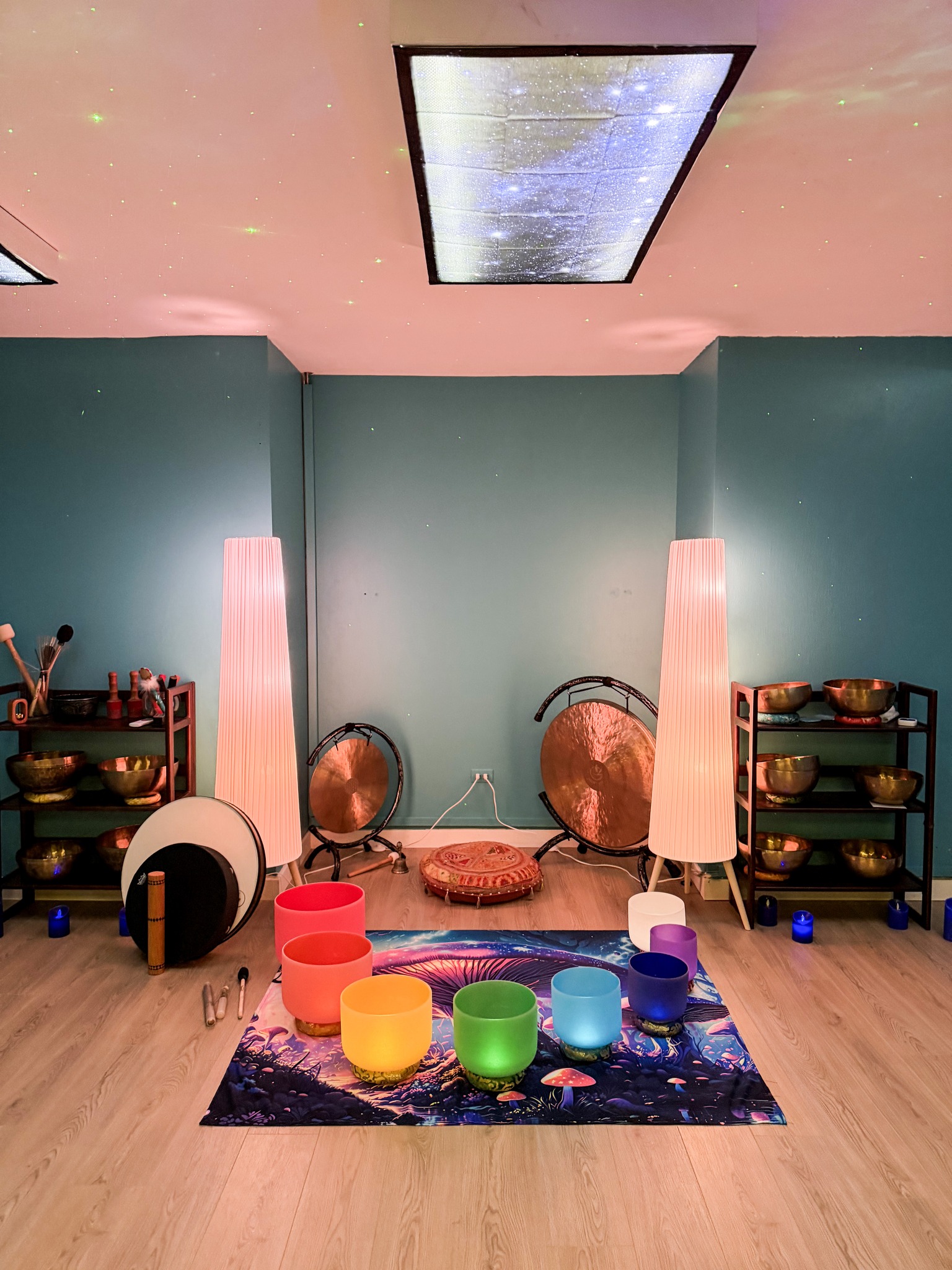 Room with teal walls, pink ceiling, two tall lamps, musical instruments, colorful bowls on a rug, and a ceiling with a starry sky projection.