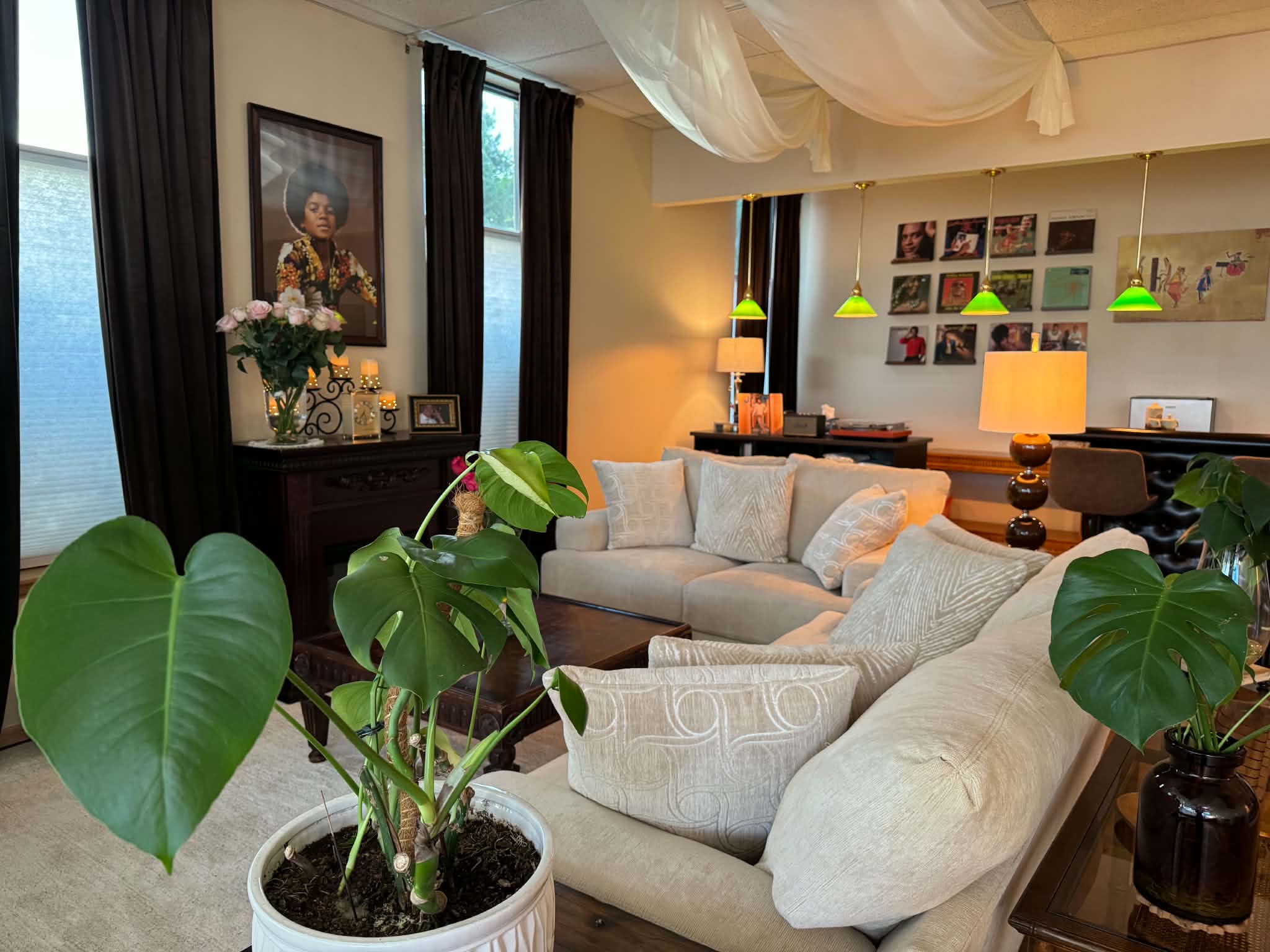 Living room with beige sofas, green plants, artwork, and colorful pendant lights, decorated with flowers and lamps.