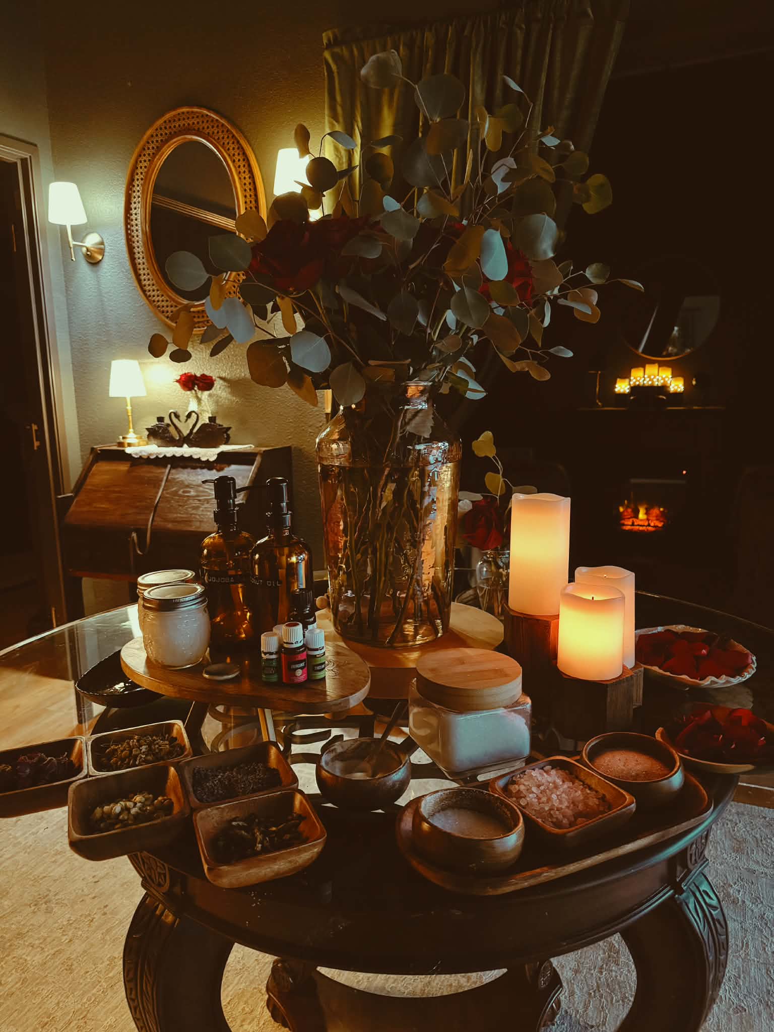 A table with a large flower arrangement, candles, and various food items in a dimly lit room.
