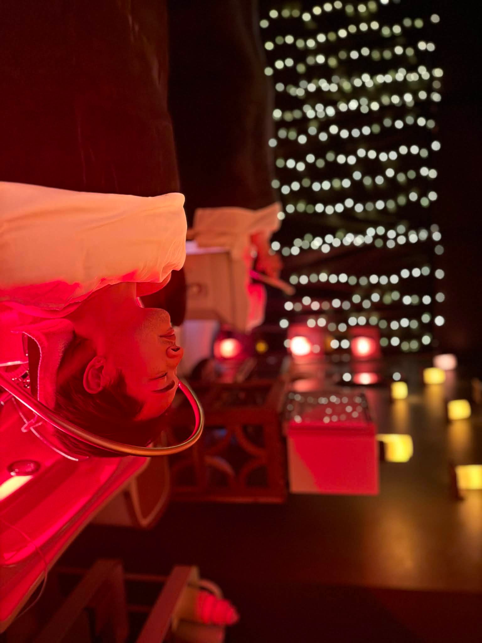 Person lying on a bed with eyes closed in a dimly lit room with string lights and warm lighting