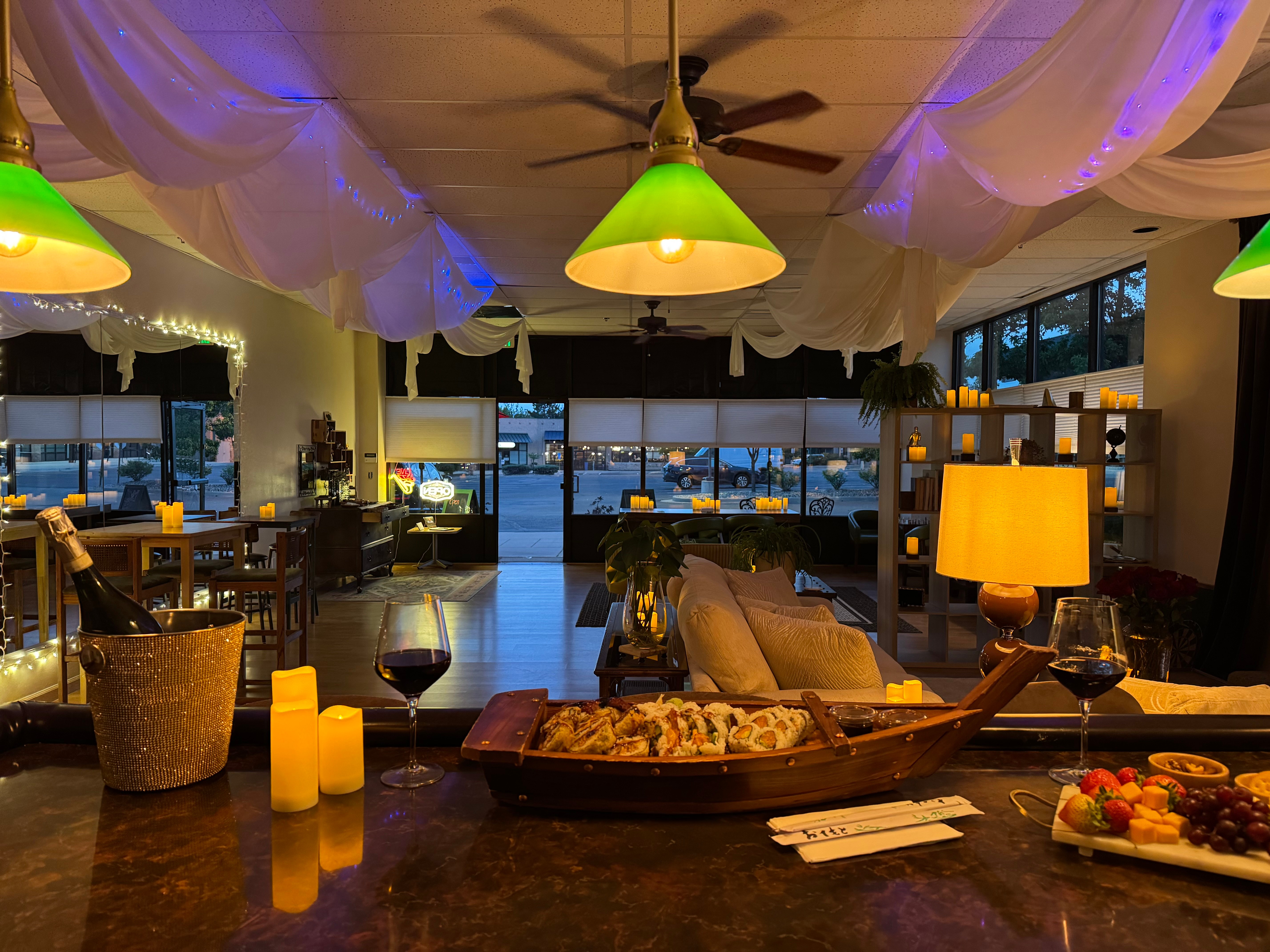 Indoor dining area with large windows, hanging lights, and a view of water outside, decorated with candles and plants.