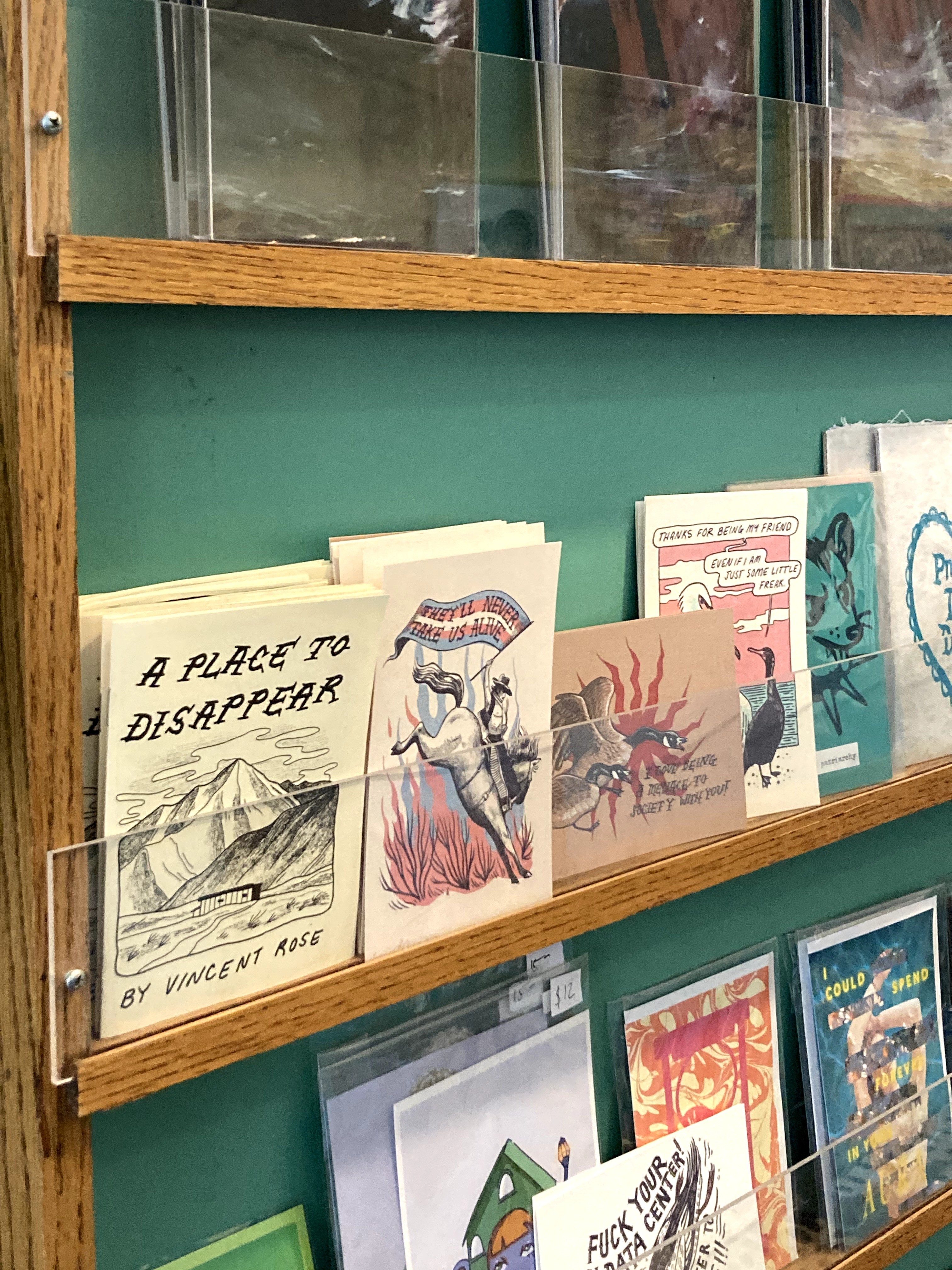 Books displayed on a wooden shelf against a green wall, with titles and illustrations visible.