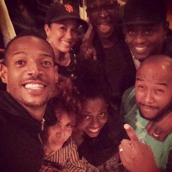 Group of seven smiling people taking a selfie indoors, some wearing hats, close together, warm lighting.