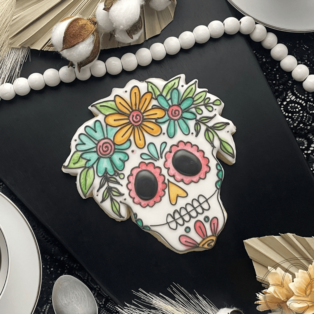 Colorful sugar skull decorated with flowers and leaves, placed on a black surface with decorative items around.