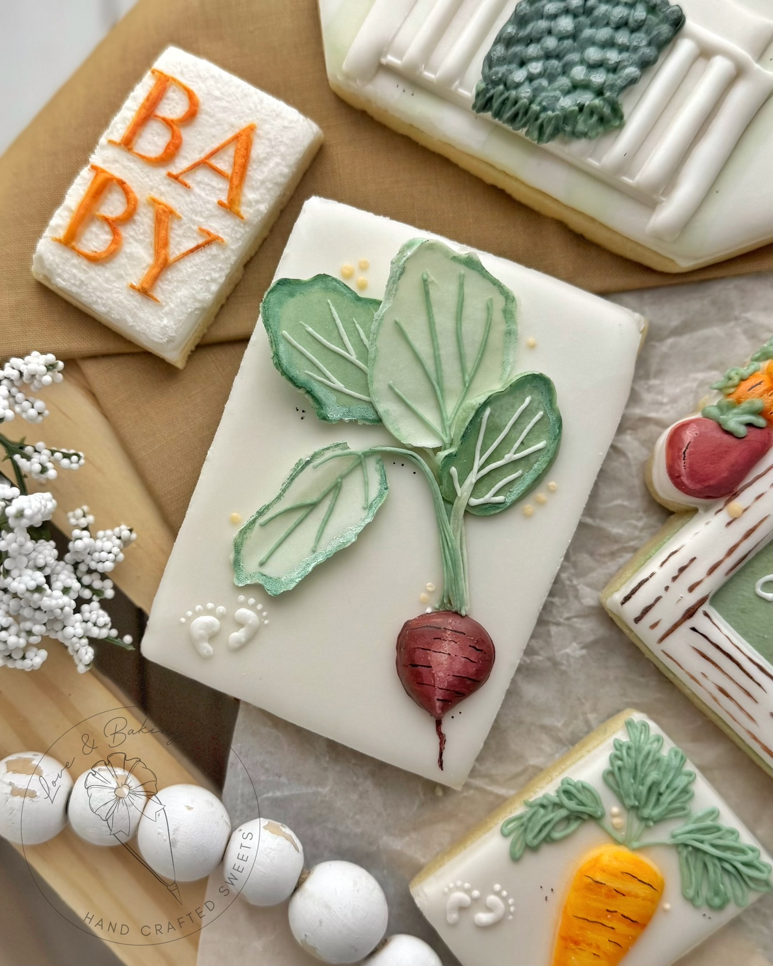Decorative soap with a radish and leaves design, surrounded by other soaps and a towel with 'BABY' embroidered, on a beige surface.