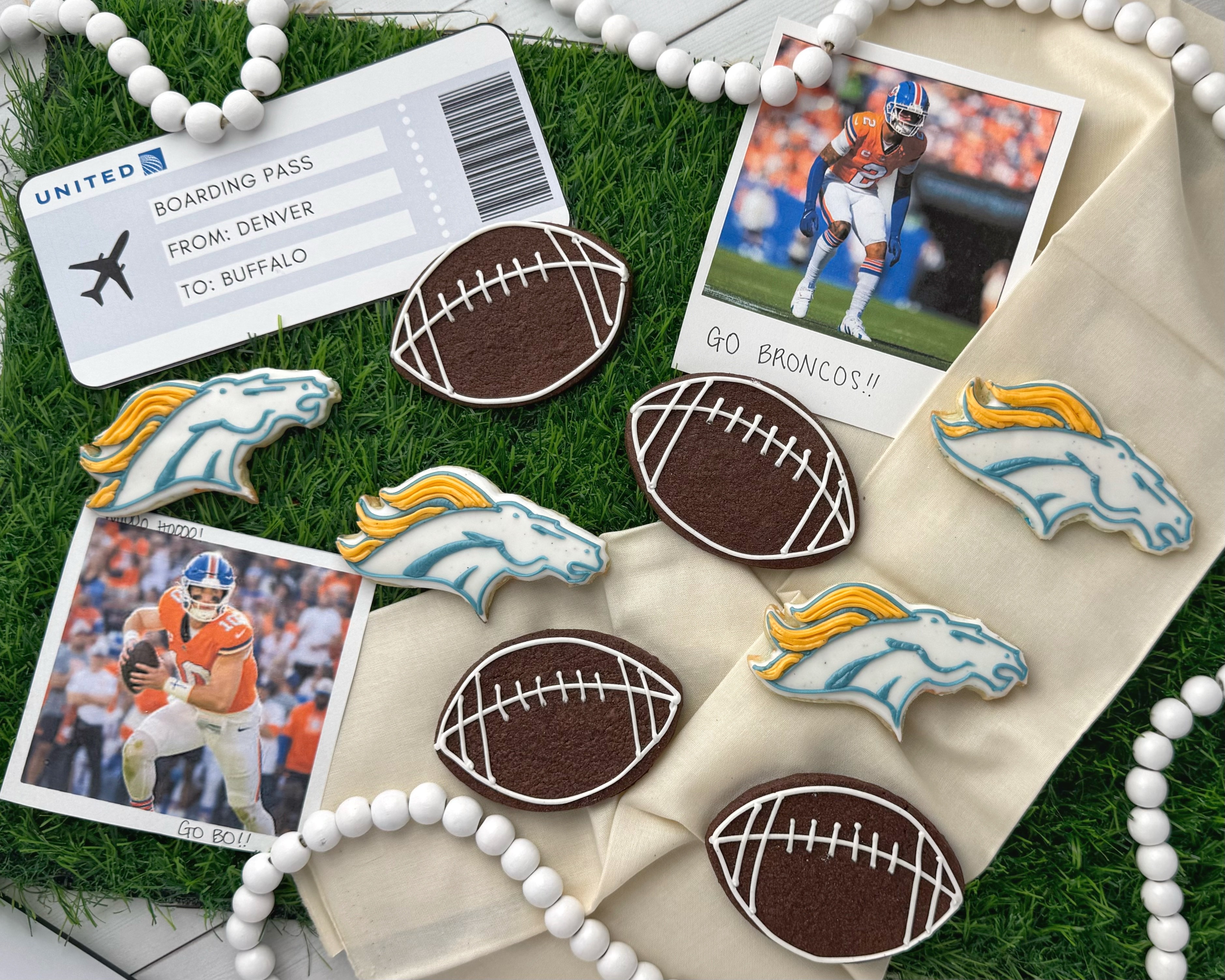 Football-themed decorations with Denver Broncos and Buffalo Bills images, tickets, and beads on grass and fabric, celebrating football game.