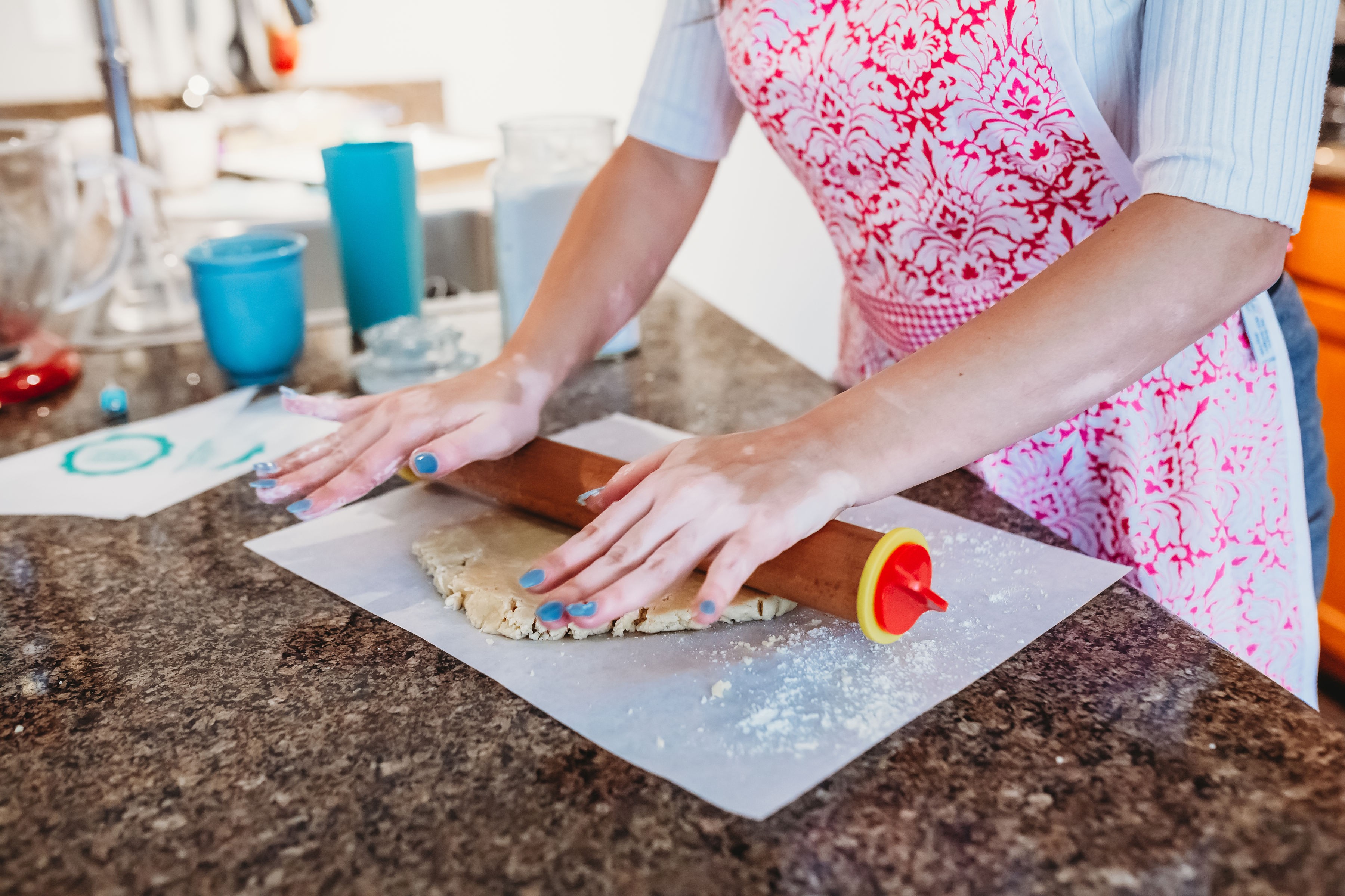 Person rolling out dough on a countertop with a rolling pin, wearing a pink apron, in a kitchen setting.