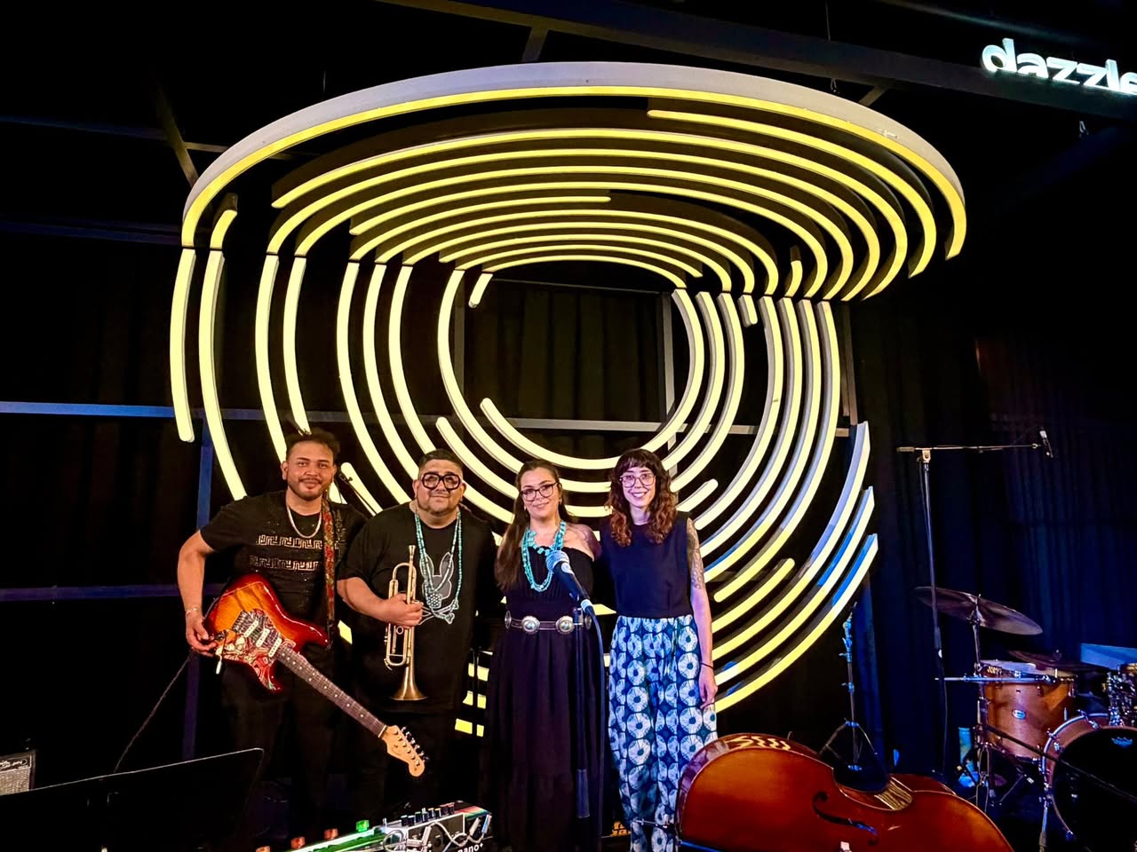 Four people stand in front of a large, illuminated spiral art installation at night, smiling and posing for the photo.